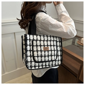 Detail of checkered tweed tote bag featuring leather logo patch and black textile handles