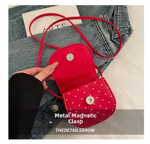 Detail of red mini crossbody bag featuring white heart prints and metal magnetic closure