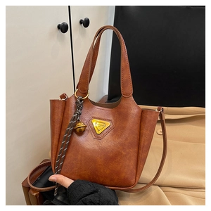 Detail of retro brown leather tote bag with gold metal plate and decorative charm
