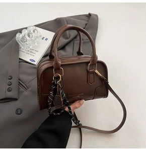 Dettaglio borsa a bauletto in pelle marrone scuro con ciondolo a racchetta e tracolla