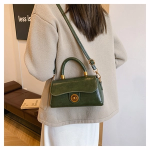 Detail of vintage dark green leather handbag featuring a round gold twist lock and top handle