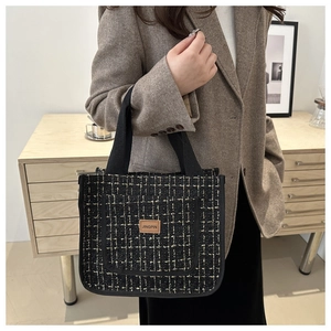 Close-up of black and gold tweed tote bag featuring a leather logo patch and woven handles