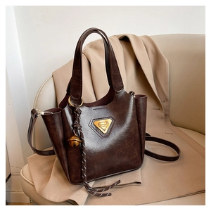 Close-up of retro brown tote bag with golden triangle logo and bell charm on beige seat