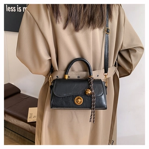 Detail view of black leather handbag with gold ring lock and woven rope handle charm