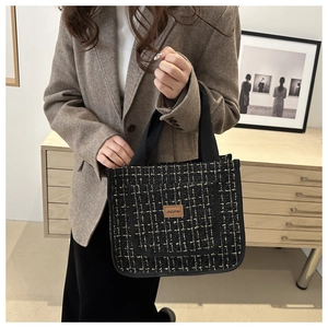 Detail of black tweed tote bag featuring gold metallic threads and a leather brand patch
