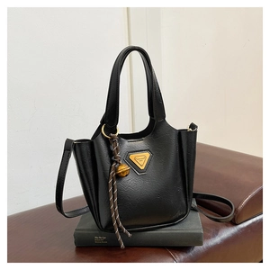 Close-up of black glossy leather tote with gold logo and decorative ball charm