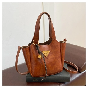 Detailed close-up of brown vintage leather tote bag with metal logo and bell charm accessory