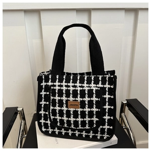 Detail of checkered tote bag with woven handles and brown leather logo patch