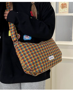 Detail of red and blue houndstooth crossbody bag with wide shoulder strap and fabric label