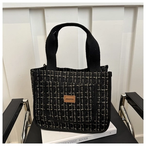 Detail shot of black tweed tote bag texture with elegant gold thread and leather label