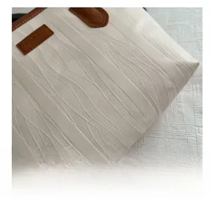 Detail of white leather tote bag with woven texture and brown leather label branding