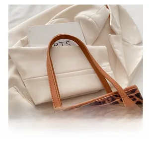Detail shot of leopard print tote bag with brown leather straps on a white blazer background