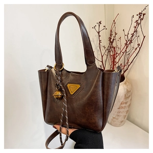 Close-up of vintage brown tote bag with metal logo, bell pendant and fine leather texture