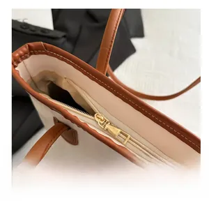 Detailed close-up of a smooth gold metal zipper on a large beige tote bag with brown trim