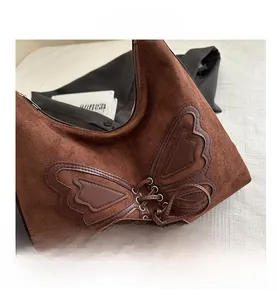 Detail of brown suede shoulder bag featuring retro butterfly patch and leather lace-up