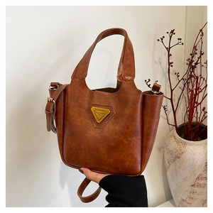 Close-up of vintage brown leather tote bag with gold metal logo and adjustable strap