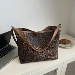 Leopard print tote bag with brown leather trim displayed on a white desk for work