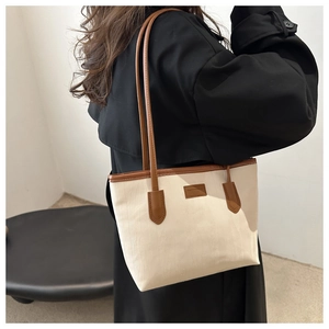 Close-up of cream canvas tote bag with brown leather trim worn with a black coat