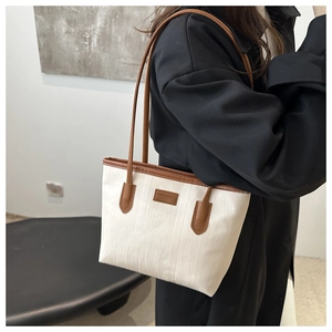 Close-up of minimalist cream tote bag with wave texture and brown leather strap detail