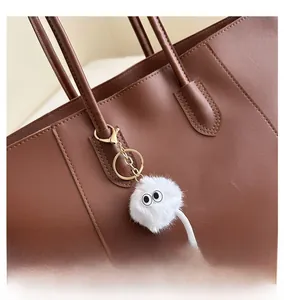Close-up of white plush monster charm with big eyes on a brown leather handbag