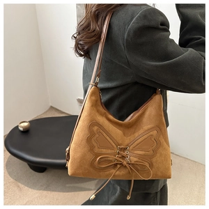 Detail view of caramel suede bow shoulder bag with woven textures worn by model