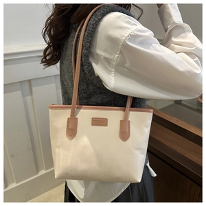 Detail of minimalist cream canvas tote bag with pink leather handles and branded patch