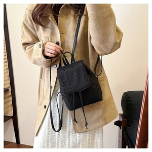 Close-up of a mini black fuzzy backpack with drawstring and flap closure on a model