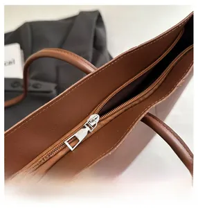 Close-up of smooth silver metal zipper on a dark brown leather tote handbag for women