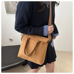 Brown suede tote bag with leather handles and crossbody strap on a model wearing casual outfit