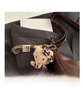 Detailed view of plush cat charm in leopard print outfit on a brown leather tote bag