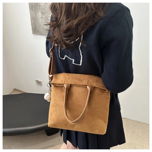 Detailed side view of brown suede tote bag featuring baseball charm and adjustable strap