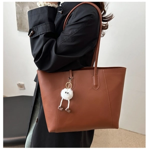 Detailed view of brown leather tote bag featuring a cute white plush pendant accessory