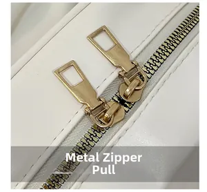 Detailed macro view of durable gold metal zipper pulls on a white leather backpack