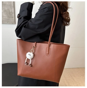 Close-up of brown PU leather tote bag with vertical stitching and a cute plush charm