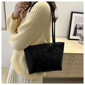 Detail of black tote bag featuring fine grain texture and fashion logo on model