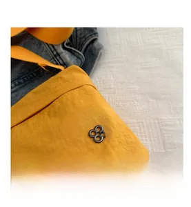 Close-up of yellow nylon crossbody bag with textured fabric and black metal logo detail