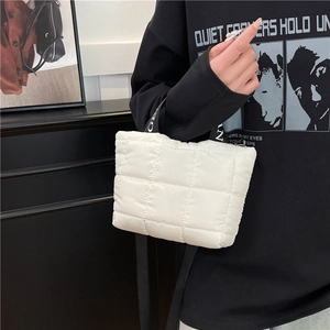 White quilted puffer handbag with letter strap held by a person in a minimalist style
