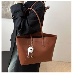 Detail view of brown matte leather tote bag with a white fluffy monster charm