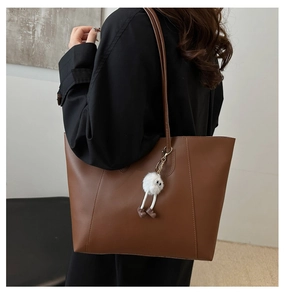 Detail of dark brown leather tote bag with a white plush monster charm on shoulder