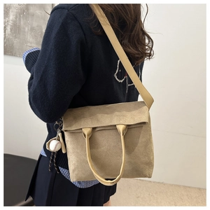 Detail view of khaki suede tote bag featuring a round handle and baseball charm ornament