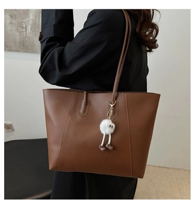 Brown faux leather tote bag with white plush charm worn by model in a minimalist setting