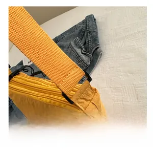 Close-up of yellow nylon crossbody bag showing black buckle detail and wide shoulder strap