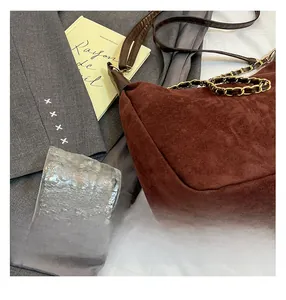 Deep brown suede shoulder bag with metal chain strap displayed on grey blazer background
