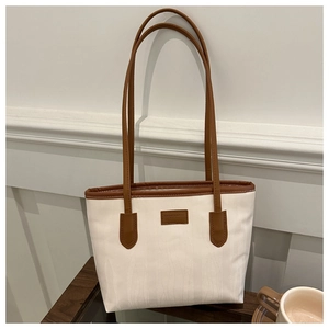 Close-up of white canvas tote bag with brown leather handles and fashion logo details