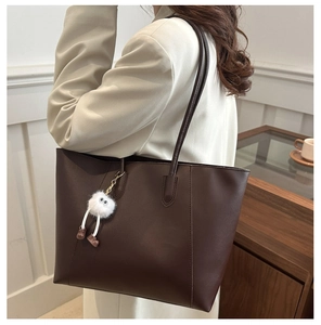 Deep brown tote bag with plush charm shown in a cozy indoor setting for size reference