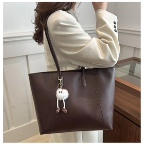 Deep brown leather tote bag detail with a cute white plush doll keychain accessory