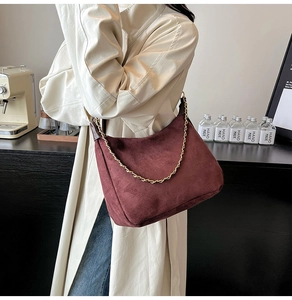 Close-up of a burgundy suede half-moon shoulder bag with an elegant gold chain strap