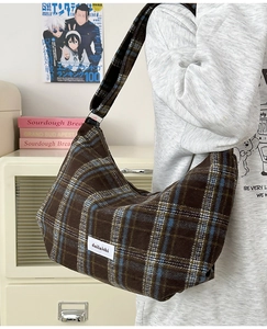 Detailed close-up of brown plaid hobo bag with white brand label and soft fabric texture