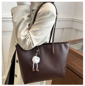 Detail of dark brown tote bag featuring a cute white plush monster charm on shoulder strap