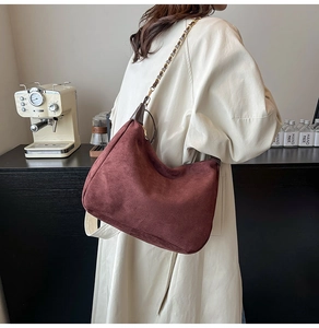 Detail of burgundy suede hobo bag with metal chain strap and leather stitching